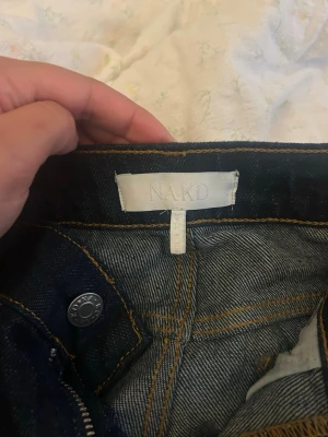 Mörkblå bootcut jeans från NA-KD - Säljer ett par mörkblå bootcut jeans från NA-KD med klassiska fem fickor och snygga kontrastsömmar. Jeansen har hög midja och utsvängda ben, perfekta för en trendig och avslappnad look. Materialet är kraftig denim i bomull.