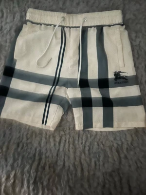 Vita rutiga shorts med snörning - Snygga vita shorts med klassiskt rutigt mönster i svart och grått. Shortsen har elastisk midja med snörning och sidofickor. Perfekta för sommaren eller badhuset och ger en stilren vibe till din outfit.