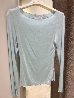 Ljusblå topp intimissimi liknande  - Säljer en ljusblå långärmad topp från Gina Tricot. Toppen har en enkel och stilren design med rund halsringning och är tillverkad i ett mjukt, stretchigt material som sitter snyggt på kroppen. Perfekt att matcha med jeans eller kjol.
