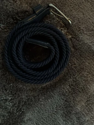 Mörkblått flätat bälte med metallspänne - Snyggt mörkblått bälte i flätad design med ett stilrent metallspänne. Perfekt för att ge din outfit en clean och modern touch. Bältet är flexibelt och passar till många olika looks.