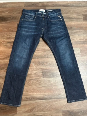 Mörkblå raka jeans från Replay - Snygga mörkblå jeans från Replay med raka ben och klassisk femficksmodell. Jeansen har kontrastsömmar, dragkedjegylf och detaljerade bakfickor. Tillverkade i slitstark denim som passar perfekt till en avslappnad stil.