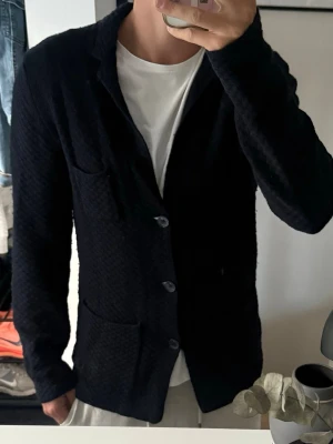 Marinblå stickad kofta från Massimo dutti - Marinblå stickad kofta från Massimo duttil. Kavajen har tre fickor, varav en bröstficka och två framtill. Passar perfekt till en avslappnad men ändå stilren look. Materialet ser mjukt och bekvämt ut. Ganska nopprig och har ett litet hål där bak vid kragen som man ser på sista bilden 