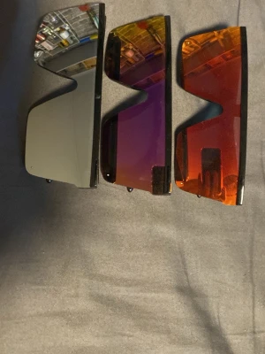 Tre par futuristiska solglasögon - Säljer tre par solglasögon med futuristisk vibe och rektangulära, spegelblanka glas i silver, lila och orange. Alla har svarta bågar och stora linser som täcker mycket av ansiktet. Perfekta för dig som vill sticka ut och addera färg till din stil.