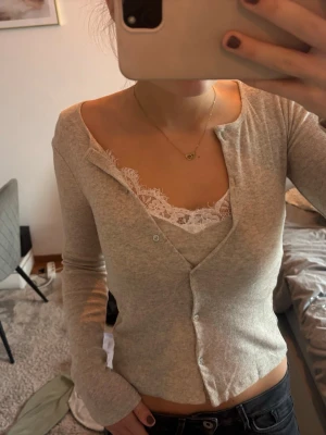 Spetskofta från Zara - Supersnygg beige kofta med ribbad struktur och v-ringning. Koftan har knäppning framtill och långa ärmar. Under syns ett vitt linne med spetskant som ger en extra touch till looken. Perfekt att styla med jeans eller kjol.
