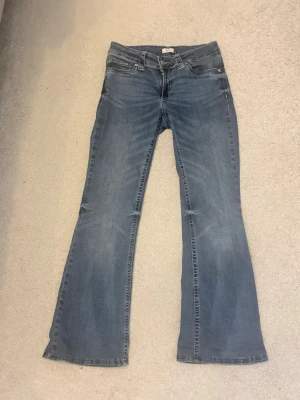Blå bootcut jeans med mönstrade fickor OBS: dem har blivit kortare för att passa tjejer 150-157cm - Säljer ett par blå bootcut jeans med coola vita mönster på bakfickorna. Jeansen har klassisk femficksdesign, normalhög midja och är tillverkade i denim. Perfekta för dig som gillar en avslappnad men trendig look.