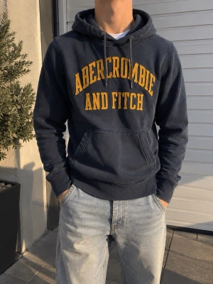 Abercrombie & Fitch Navy Hoodie – Y2K - Snygg navy hoodie från Abercrombie & Fitch med klassiskt stort broderat tryck framtill.  Vintage/Y2K-känsla och riktigt lätt att matcha. Bra skick och perfekt för en clean, avslappnad stil.  📦 Skickas snabbt och packas noggrant!