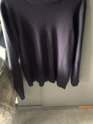 Mörkblå stickad tröja - En enkel och stilren mörkblå stickad tröja med rund halsringning och långa ärmar. Tröjan har en klassisk rak passform och är ribbstickad i mjukt material, perfekt för kyligare dagar.