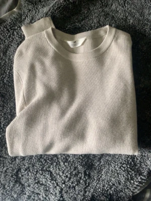 Beige ribbstickad tröja - En stilren beige ribbstickad tröja med rund hals och långa ärmar. Tröjan har en enkel och klassisk design som passar till det mesta. Materialet ser mjukt och bekvämt ut, perfekt för lager på lager under kyligare dagar.