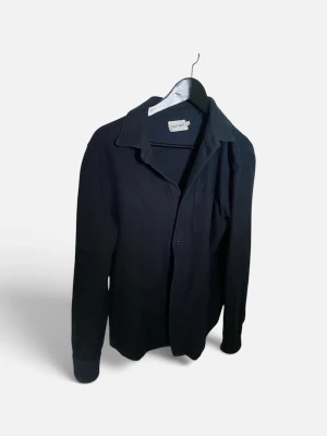 Blå overshirt från East West - Stilren blå overshirt från East West med klassisk krage och knäppning framtill. Overshirten har långa ärmar och en bröstficka, perfekt för en avslappnad men snygg look. Materialet ser ut att vara mjukt och bekvämt.