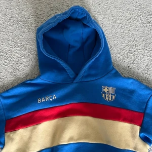 Blå Barça hoodie med röd och beige rand - En Barcelona tröja från 2022 som är väldigt snygg. Använd 2-3 gånger väldigt bra skick. Säljer för 300 kr! Möjligtvis kan godkänna ner till 180 kr!