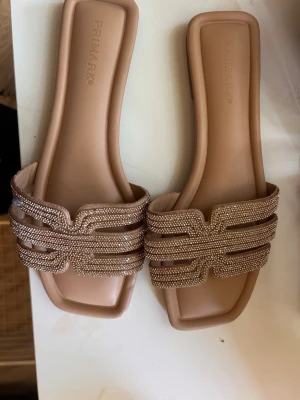 Glittriga guldiga sandaler  - Snygga beige sandaler från Primark med fyrkantig tå och breda remmar täckta av glittrande strass. Mjukt innersula för extra komfort och platt sula. Perfekta för att addera lite bling till din outfit.