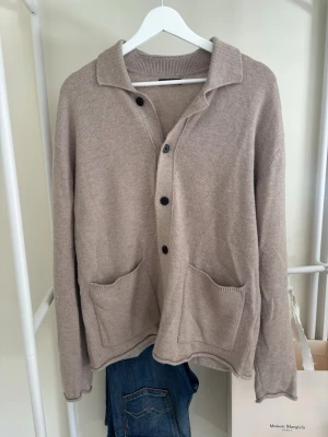 Beige kofta med fickor och krage - Snygg beige kofta från Massimo dito med avslappnad passform, krage och svarta knappar framtill. Tillverkad i mjukt stickat material, perfekt för lager på lager. Långa ärmar och enkel design som passar till det mesta.
