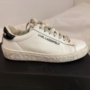 Vita sneakers från Karl Lagerfeld - Intressekoll på mina vita sneakers från Karl Lagerfeld med silverfärgad logga på sidan och präglad text på sulan. Skorna har snörning, svart detalj på hälen och är tillverkade i skinn. 