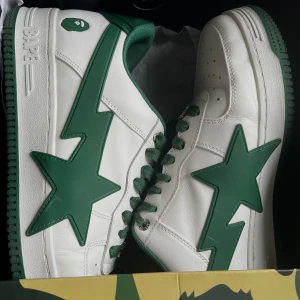 BAPE STA vita och gröna sneakers - Säljer ett par BAPE STA sneakers i vitt och grönt skinn med ikonisk stjärndesign på sidorna. Skorna har gröna snören, grönt innerfoder. Kommer med originalkartong och dustbag med BAPE-logga och ett par vita skosnören. Perfekta för dig som gillar streetwear. Storlek 43/44