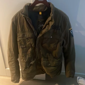 Olivgrön fieldjacket från Marc o polo - Säljer en olivgrön parkajacka från MacGregor med flera fickor framtill och coola patchar på ärmen. Jackan har dragkedja och knappar, samt en klassisk parkalook som funkar perfekt till jeans och hoodie. Materialet är slitstark polyester.