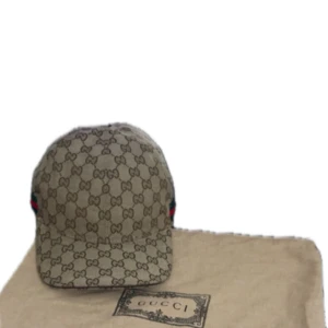 Beige GG-mönstrad keps från Gucci - Snygg beige keps från Gucci med klassiskt GG-monogram över hela kepsen. Justerbar rem bak i mörkbrunt skinn och diskreta gröna och röda detaljer på sidorna. Tillverkad i bomullscanvas med exklusiva skinninslag. Perfekt för dig som vill sticka ut med en lyxig accessoar.
