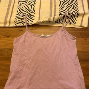 Ljuslila linne från NA-KD - Säljer ett ljuslila linne från NA-KD med tunna axelband och enkel, rak passform. Toppen är tillverkad i mjuk bomull och passar perfekt till sommaren. Stilren och enkel att matcha med olika outfits.