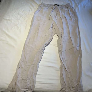 Beiga linnebyxor med snörning - Luftiga och sköna beiga linnebyxor med resår och snörning i midjan. Perfekta för varma dagar och har en avslappnad passform. Byxorna har raka ben och är tillverkade i ett lätt och svalt linnematerial.