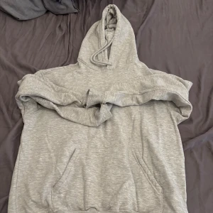 Grå hoodie med huva och ficka - En klassisk grå hoodie med huva och snörning samt en stor magficka framtill. Tröjan har långa ärmar och är tillverkad i mjukt material, perfekt för chill dagar eller när du vill ha något bekvämt på dig. Från HM storlek S
