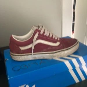 Vinröda Vans Old Skool sneakers - Säljer ett par klassiska Vans Old Skool sneakers i vinrött med vit sula och vit sidostrip. Skorna har snörning och rund tå, ovandel i skinn och textil samt ikonisk Vans-logga på sidan. Perfekta för dig som gillar streetstyle och skatevibe.