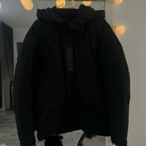 Svart pufferjacka från Hoodrich S - Säljer en svart pufferjacka från Hoodrich i storlek S. Jackan har huva, dragkedja och tryck med text både fram och bak. Snygg med stora fickor och detaljerade tryck. Perfekt för kalla dagar när du vill ha en stilren vibe. Jackan är använd ett par gånger.