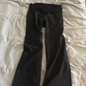 Svarta bootcut byxor med spetsdetalj från design by si  - Svarta byxor med bootcut-snitt och bred spetskant i midjan från design by si Snygg och unik detalj som ger extra edge till outfiten. Byxorna har en klassisk passform och är tillverkade i ett mjukt, följsamt material som sitter skönt hela dagen. Storlek L men sitter som M