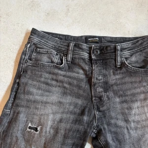 Grå slitna jeans från Jack & Jones - Säljer ett par grå jeans från Jack & Jones med snyggt slitna detaljer, Klassisk, Perfekta för dig som gillar en avslappnad och trendig stil.