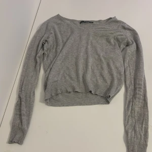 Grå stickad tröja från 157, XS - En enkel och stilren grå stickad tröja från 157 i storlek XS. Tröjan har v-ringning, långa ärmar och ribbade muddar vid ärmslut och nederkant. Perfekt för lager-på-lager och passar till allt.