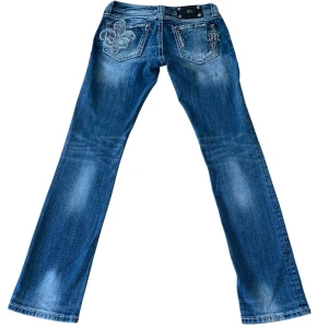 Vintage low waisted Miss Me straight jeans med broderi - Snygga blå Miss Me jeans i straight fit med broderade bakfickor och nitar. Jeansen har coola detaljer som dekorativa sömmar, broderat mönster och logga på bakfickan. Tillverkade i bomull med lite stretch för skön passform.