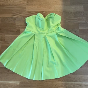 Limegrön axelbandslös klänning från ASOS - Superfin limegrön axelbandslös klänning från ASOS med utsvängd kjol och snygga veck framtill. Klänningen har en cool offshoulder-look och är perfekt för dig som vill sticka ut med en färgstark stil. Materialet känns slätt och har en lätt glans.