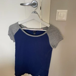Blå och grå t-shirt från U.S. Polo Assn. - T-shirt från U.S. Polo Assn. i storlek S med marinblå framsida och grå ärmar. Klassisk rund halsringning och korta ärmar. Tillverkad i mjuk bomullsmix för en skön känsla. Perfekt för en avslappnad och sportig look.