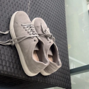 Grå mockasneakers med snörning - Snygga grå sneakers i mocka med klassisk design och vita sulor. Skorna har rund tå, platt sula och snörning framtill. Perfekta för en stilren och avslappnad look.