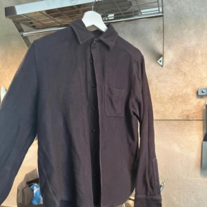 Mörkblå overshirt från East West - Säljer en mörkblå overshirt från East West i grov bomull. Skjortan har klassisk krage, bröstficka och knäppning framtill. Perfekt att slänga över en t-shirt för en chill look. Långärmad och med enkel, stilren design.