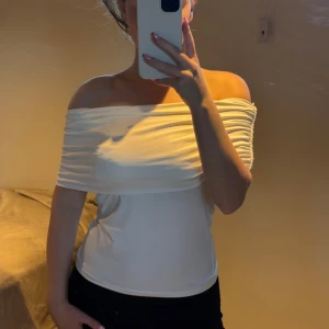Vit offshoulder topp med rynk - Säljer denna så fina vita offshoulder topp med snygga rynkade detaljer över axlarna. ✨🌸Toppen är axelbandslös och sitter tight över bysten, perfekt för en trendig look. Materialet känns mjukt och stretchigt, vilket gör den bekväm att bära.😍Prislapp kvar! 