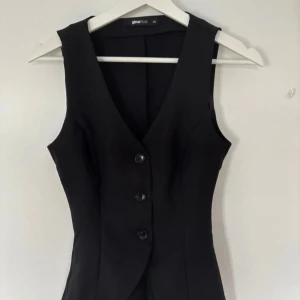 Svart väst från Gina Tricot S - Snygg svart väst från Gina Tricot i figurnära modell med tre knappar framtill och djup v-ringning. Perfekt att styla över en skjorta eller t-shirt för en trendig look. Klassisk och stilren design som passar till många outfits.
