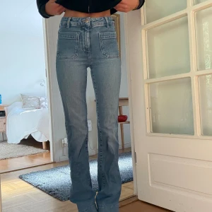 Ljusblå bootcut jeans med fickor - Snygga ljusblå jeans med bootcut och höga fickor framtill. Byxorna har hög midja och raka ben med lätt utsvängning nertill. Klassisk jeanslook med coola detaljer och sömmar, perfekta för en trendig vardagsstil.