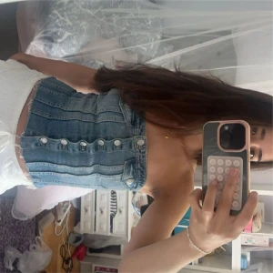 Jeans tubtopp med knappar - Säljer en snygg tubtopp i jeansmaterial med silverfärgade knappar framtill. Toppen är axelbandslös och har en croppad passform som sitter tight. Perfekt för dig som gillar denim och vill ha en cool och trendig look.