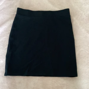 Svart kortkjol från Bik Bok - En stilren svart kortkjol från Bik Bok i storlek S. Kjolen har en enkel, rak passform och är tillverkad i mjukt och stretchigt material som sitter bekvämt. Perfekt för dig som gillar minimalistisk och clean look.