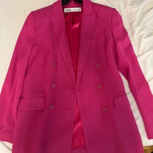 Pink ZARA Blazer - Säljer en snygg fuchsiafärgad kavaj från Zara i storlek S. Kavajen är dubbelknäppt med sex matchande knappar framtill, har klassisk krage och två fickor med lock. Fodret är i blankt tyg som matchar utsidan. Perfekt statement-plagg för dig som gillar färg.