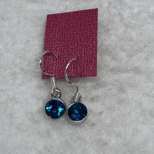 Silverörhängen med turkos sten - Snygga örhängen i silverfärg med rund, gnistrande turkos sten. Perfekta för att ge din look lite extra färg och glans. Hängande modell med enkel krok för smidig användning. Krokarna är i sterling silver. Nya