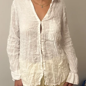 Vit linneskjorta med knappar - Säljer en luftig och stilren vit skjorta i linne med lång ärm och knappar framtill. Skjortan har en bröstficka och en avslappnad passform, perfekt för varma dagar. Materialet är lätt och ger en chill vibe.