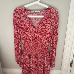 Blommig röd klänning från Zara XS - Supersöt röd klänning från Zara med blommigt mönster och v-ringad hals. Klänningen har långärmade ärmar, smockad midja och volang nedtill. Passar även en S 