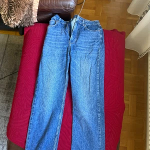 Blå jeans från Never Denim, straight fit - Klassiska blå jeans från Never Denim med rak passform och hög midja. Jeansen har fem fickor, dragkedja och knapp framtill samt snygga kontrastsömmar. 