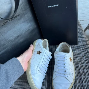 Saint Laurent vita sneakers med stjärnor - Tja! Säljer ett par feta Saint Laurent SL06 Low Top Star sneakers. I fint skick, | Storlek 39| Köpta i Italien, kvitto på sista sidan| Självklart äkta då du ser kvittot😇