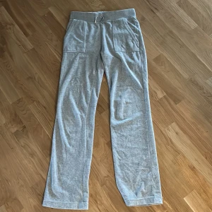 Grå mjukisbyxor Juicy Couture S - Grå mjukisbyxor från Juicy Couture med raka ben, bred resår i midjan och snörning framtill. Byxorna har stora fickor fram och bakfickor med lock och knapp. Perfekta för en chill och avslappnad look.