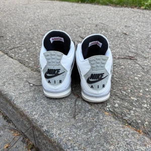 Nike Air Jordan 4 White Cement 46 - Säljer ett par Nike Air Jordan 4 White Cement i storlek 46. Klassiska sneakers i vitt skinn med grå och svarta detaljer, meshpaneler och röd Jumpman-logga på plösen. Snygg retrostil med snörning och ikonisk design – perfekta för dig som gillar streetwear.