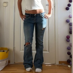 Blå bootcut jeans med slitningar - Säljer ett par blå bootcut jeans med snygga slitningar på knäna och coola detaljer på bakfickorna. Jeansen har låg midja och klassisk femficksdesign. Perfekta för dig som gillar en avslappnad och trendig look.köpta här på Plick för 900❤️ pris kan diskuteras vid snabbt köp