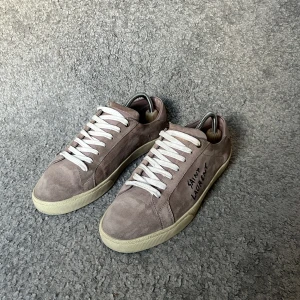 Saint Laurent sneakers - Säljer ett par snygga Saint Laurent sneakers i beige mocka med vit sula och vita snören. Inget OG tillkommer. Skorna är i princip i ny skick och endast använda ett fåtal gånger. perfekta för dig som gillar stilrena och exklusiva skor.