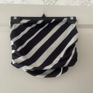 Svartvit randig Tubtopp  - Säljer en svartvit Tubtopp med breda diagonala ränder. Tubtoppen har en draperad look och är gjord i ett glansigt, mjukt material som känns lyxigt. Perfekt för dig som vill sticka ut med en cool och modern stil.