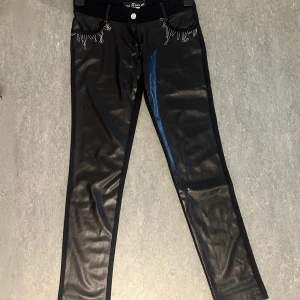 Svarta skinny byxor i skinnlook Miss Sixty - Jag säljer ett par unika byxor från butiken Ths Fashion i Grekland. De har en riktigt speciell design med skinnimitation framtill och tyg baktill. Byxorna har fina silver broderade detaljer både fram och bak. De är helt nya och aldrig använda eftersom de tyvärr inte passar mig, så de är i perfekt skick. Jag hade sagt storleken är mellan XS och S. Det här är ett plagg du inte hittar igen!